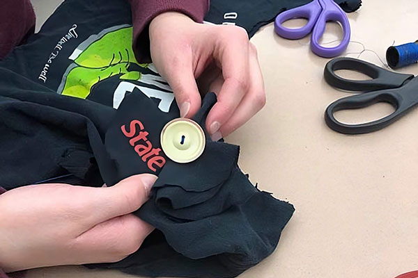A student sews a button onto a shirt.