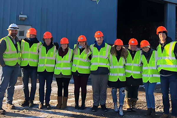 Students stand in a row wearing yellow safety vests and orange hard hats.