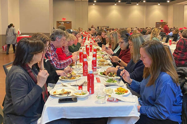 A large group of people dining at a long table with white tablecloths in a banquet room.
