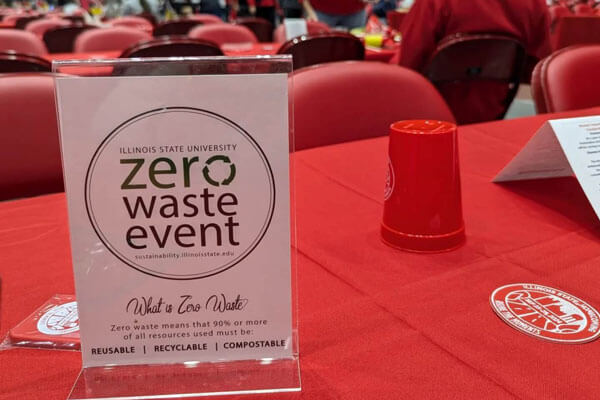 Display stand with 'Zero Waste Event' information on a red-covered table with red chairs in the background.