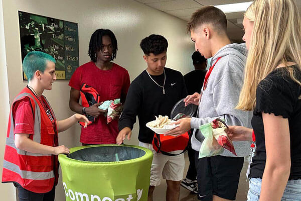 Five people in a hallway with a green compost bin.