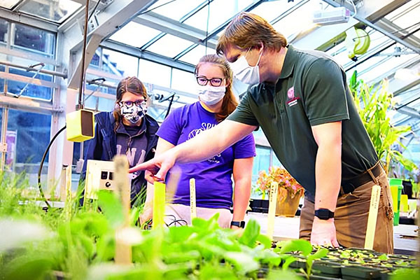 An instructor shows two students how to care for the plants inside the greenhouse.