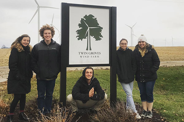 Five students stand around the Twin Groves Wind Farm sign.