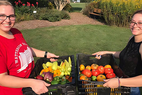 Two students hold baskets of produce they just harvested.