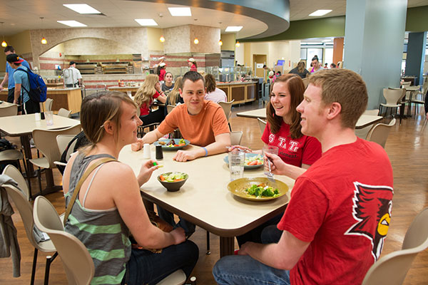 A group of students chat at a dining center table.