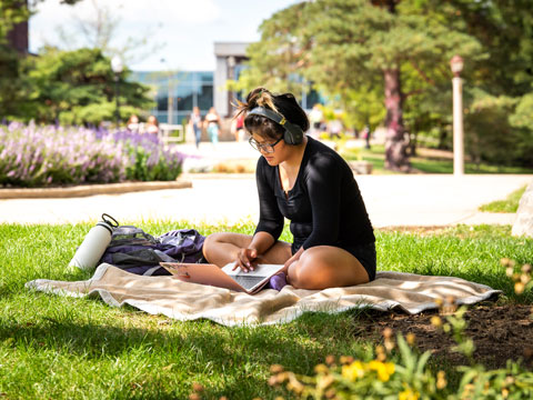 A student studies on the lawn of the quad.