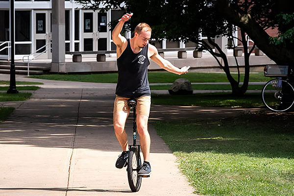 A student rides a unicycle on the quad.