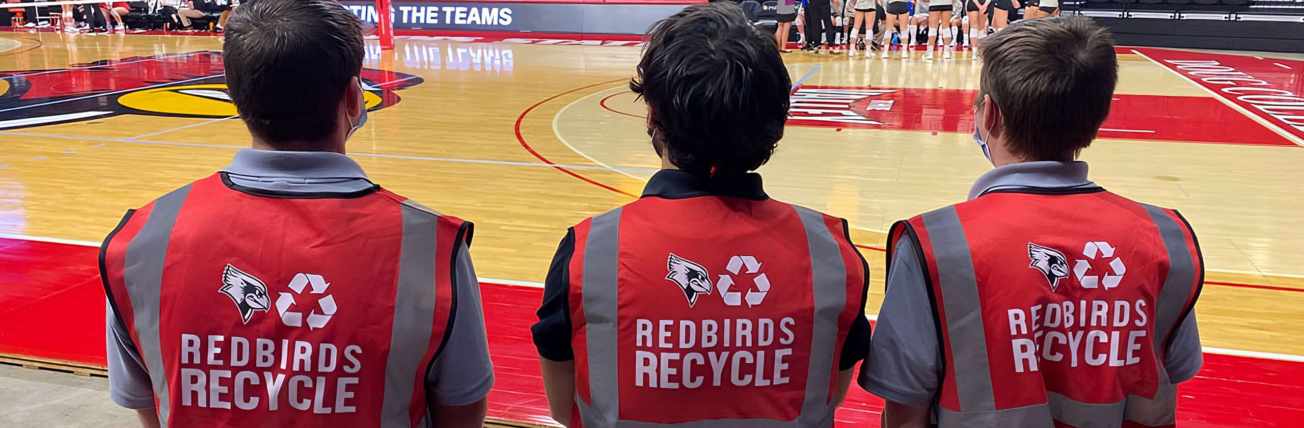 Three Redbird Recycles members stand together at a basketball game in Redbird Arena.